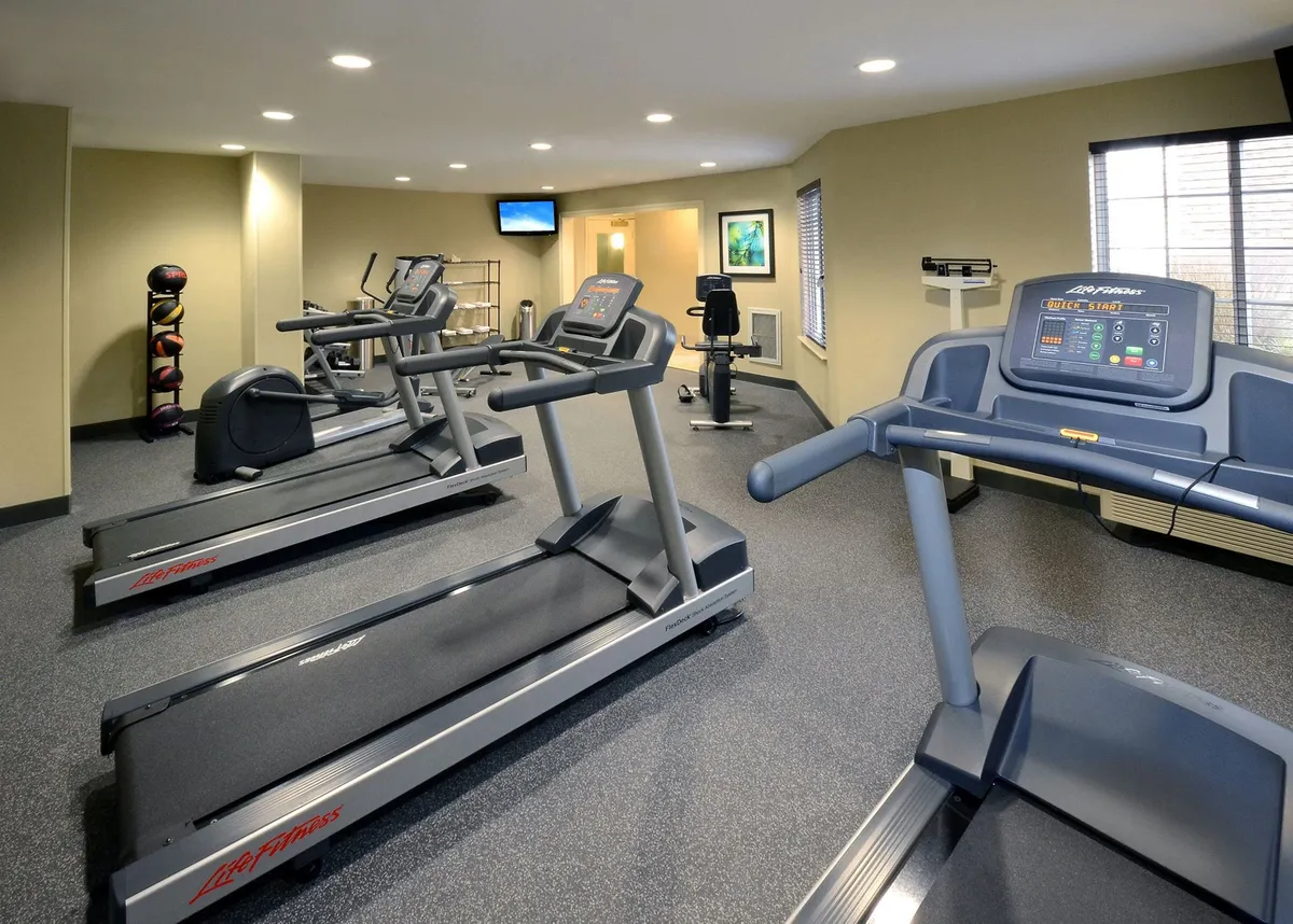 A modern fitness center equipped with several treadmills, exercise bikes, a weights rack, and a wall-mounted TV. The space is inviting and energetic, suitable for both cardio and strength workouts.
