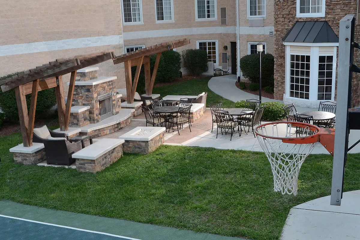 This exterior scene captures a welcoming outdoor area featuring a stone fireplace, ample seating, and a basketball hoop. The setting is ideal for social gatherings, relaxing evenings, or active family fun, with plenty of space for group activities and conversations.