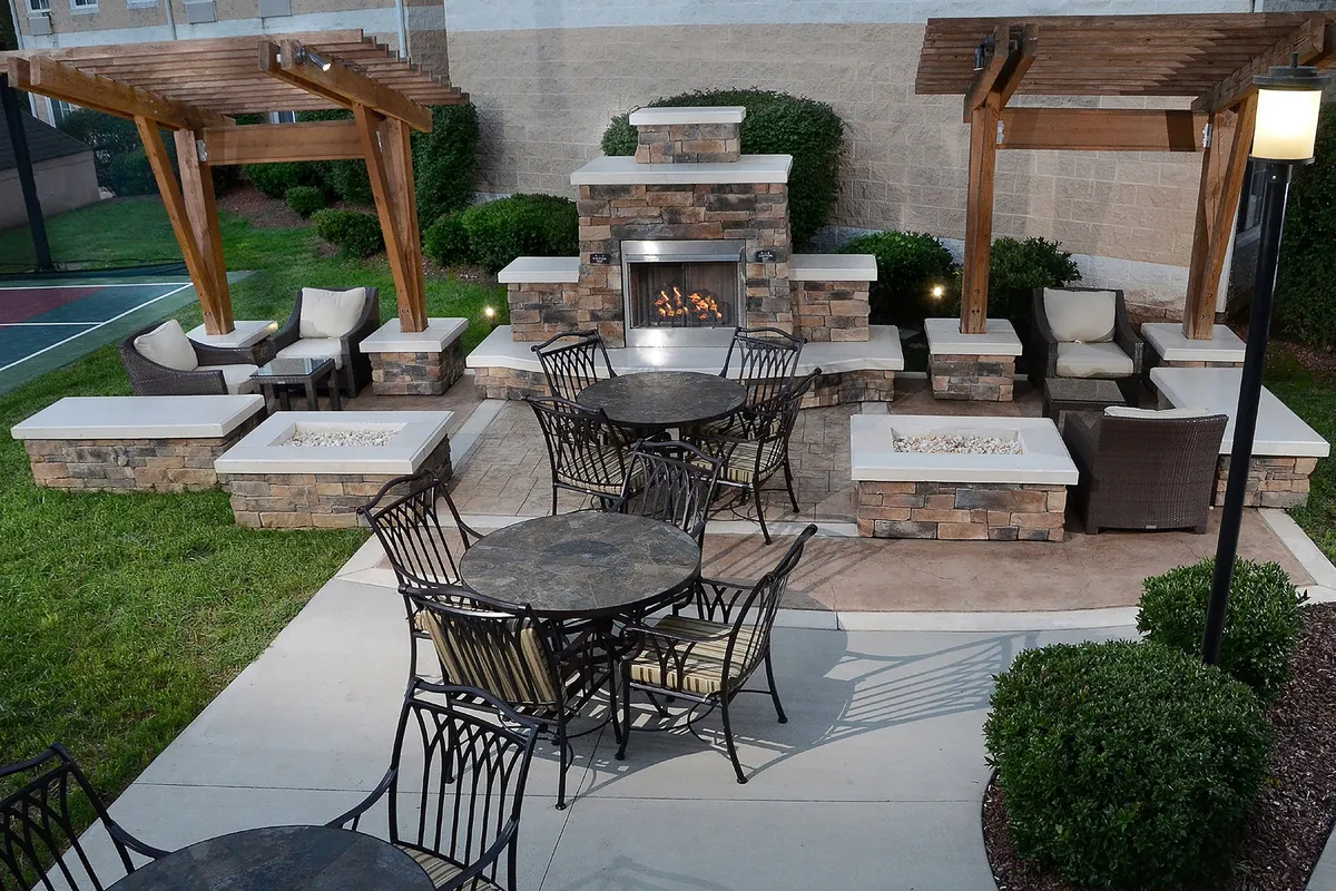 This exterior image highlights a cozy outdoor seating area arranged around a fireplace, complemented by comfortable outdoor tables and chairs. The setting invites guests to relax or socialize after a day of meetings, with warm lighting suggesting evening gatherings and a tranquil atmosphere.