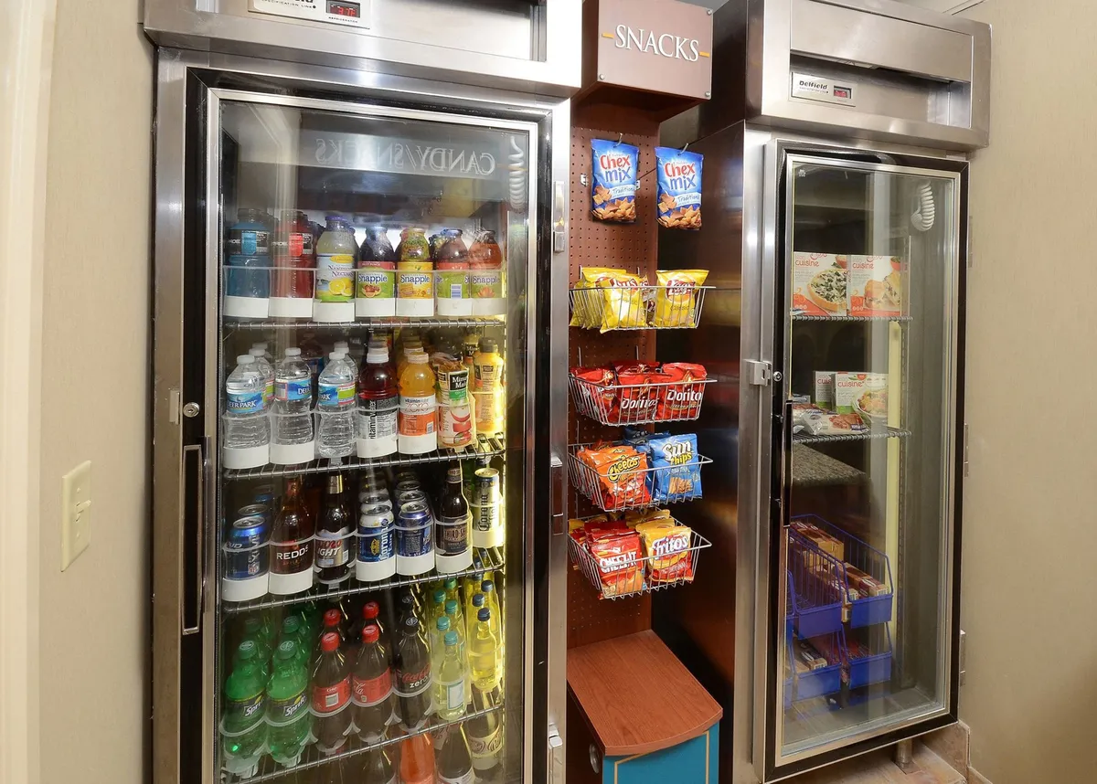 An interior scene showing a refrigerator stocked with drinks and a shelf of snacks, set in a casual, accessible area—suggestive of the convenience guests experience during extended stays.